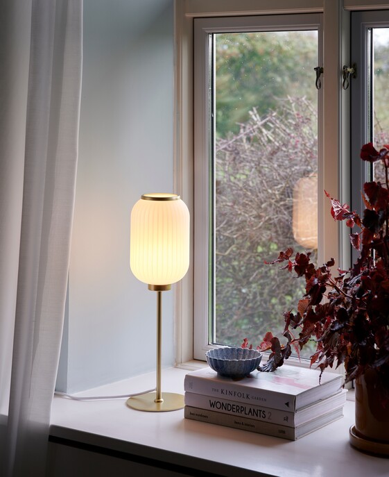 Originálnu stolovú lampičku Milford z bieleho opálového skla so skladaným vzhľadom vo vyhotovení s mosadzným podstavcom môžete mať v spálni aj vy 